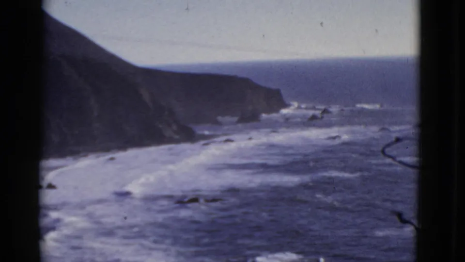 San Francisco coastal surf in a 1952 8mm frame, showing white water below a dark cliff and distant horizon.
