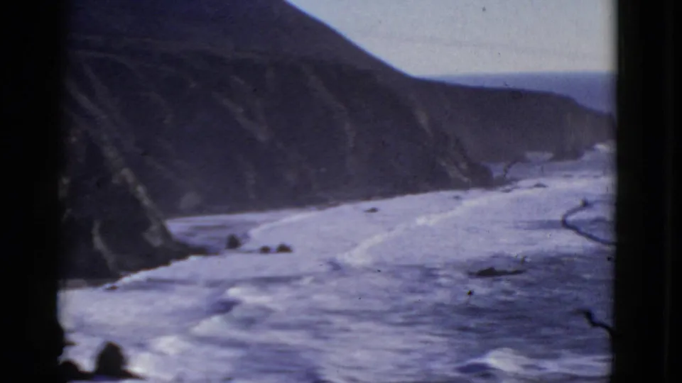 1952 home-movie frame of Pacific surf and rugged cliffs near San Francisco, with grain and soft focus from the 8mm scan.