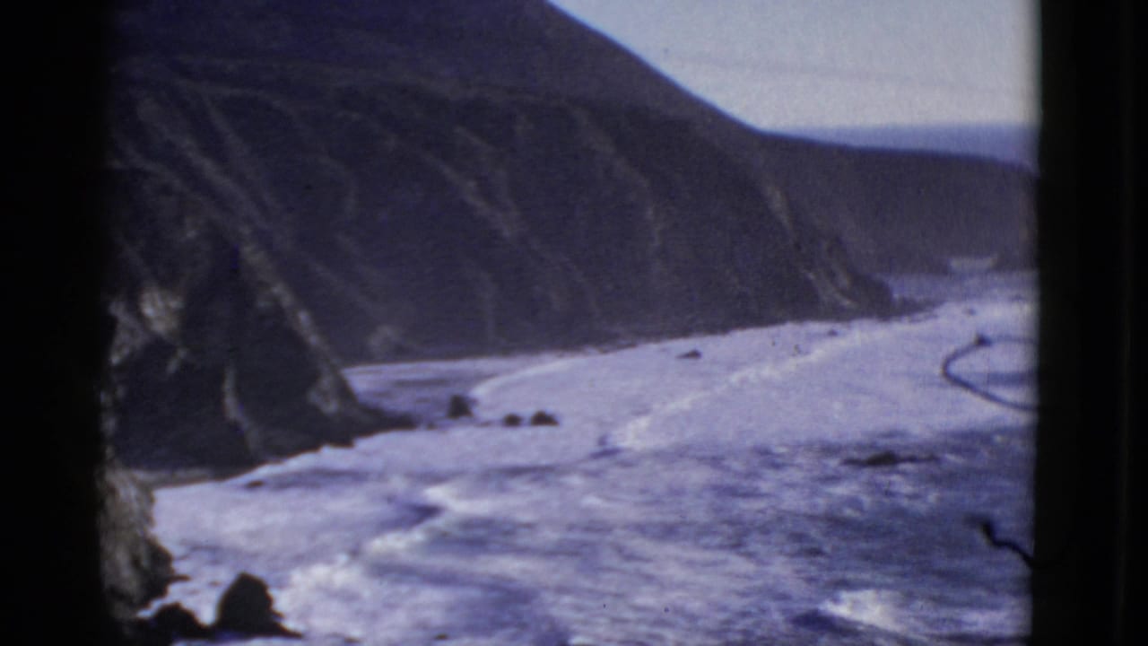1952 8mm San Francisco-area coastal view with waves below steep cliffs and dark window-like edges framing the scene.