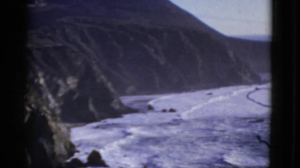 San Francisco-area shoreline appears through dark framing, with white surf tracing the base of steep coastal cliffs.