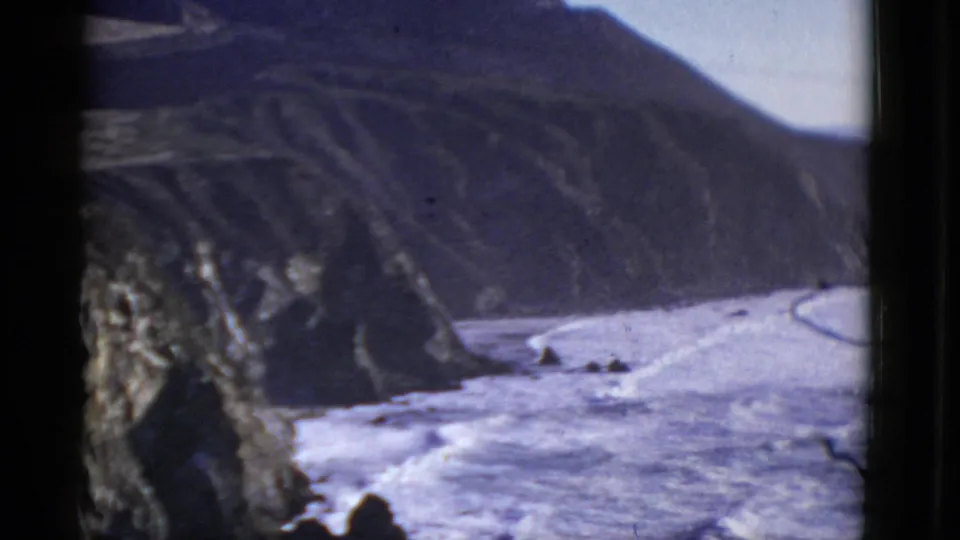 Grainy 8mm frame of a cliff face and foamy shoreline, likely from the 1952 San Francisco coastal footage.
