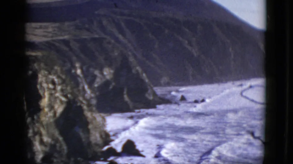 Vintage 8mm coastal frame showing surf, scattered rocks, and steep cliffs in the San Francisco-area home movie.