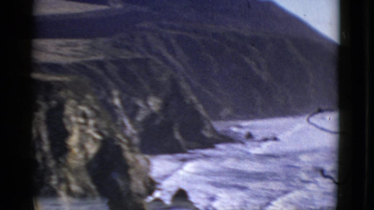1952 San Francisco coastal home-movie frame showing waves along a rocky shore beneath a shadowed cliff.