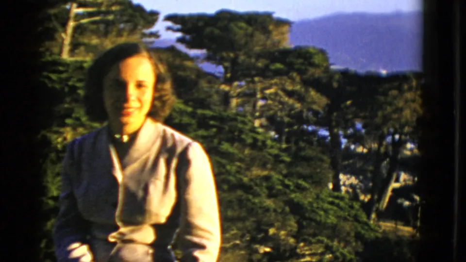 The seated woman is framed against trees, with distant water and hillside forms visible in the San Francisco background.