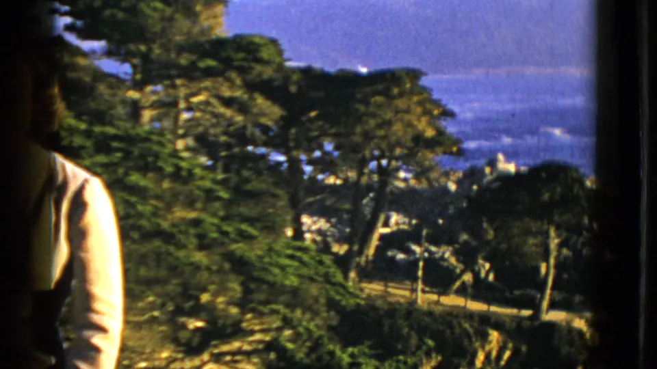 1952 San Francisco home-movie frame showing trees above the Pacific Ocean, with a partial person in a light shirt at the edge.