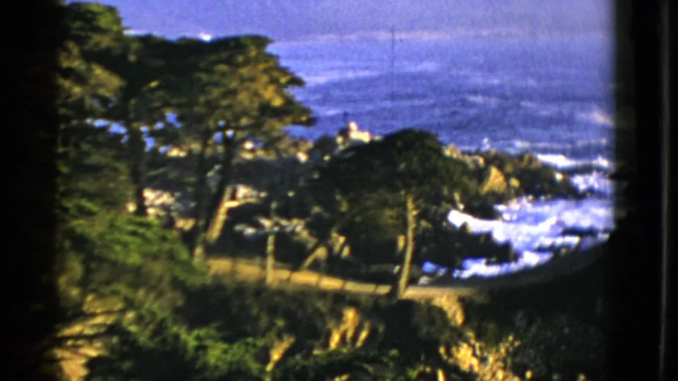 Vintage 1952 San Francisco frame showing blue ocean, white surf, rocky coast, and foreground trees from an overlook.