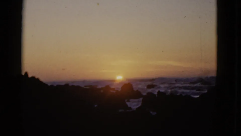1952 8mm home-movie frame showing the sun low over the Pacific, with waves breaking around silhouetted rocks near San Francisco, California.