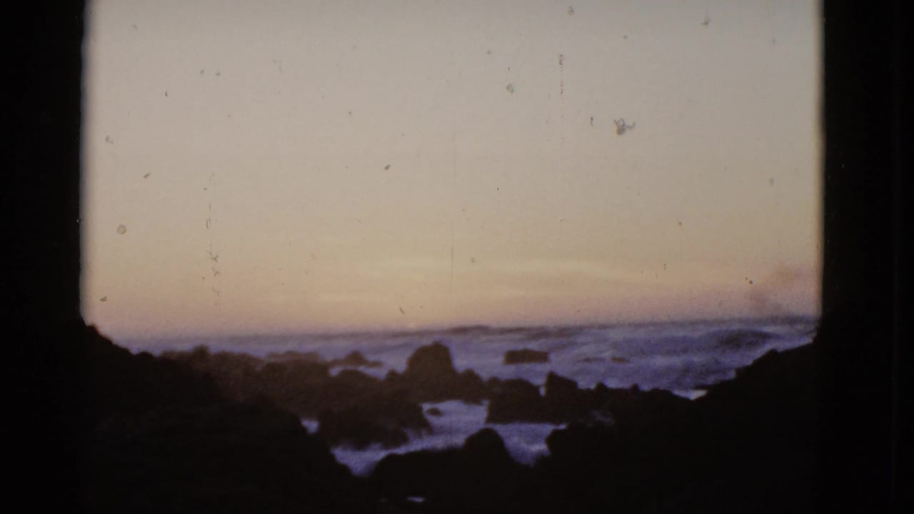 Rocky shoreline and ocean surf under a fading orange dusk sky.