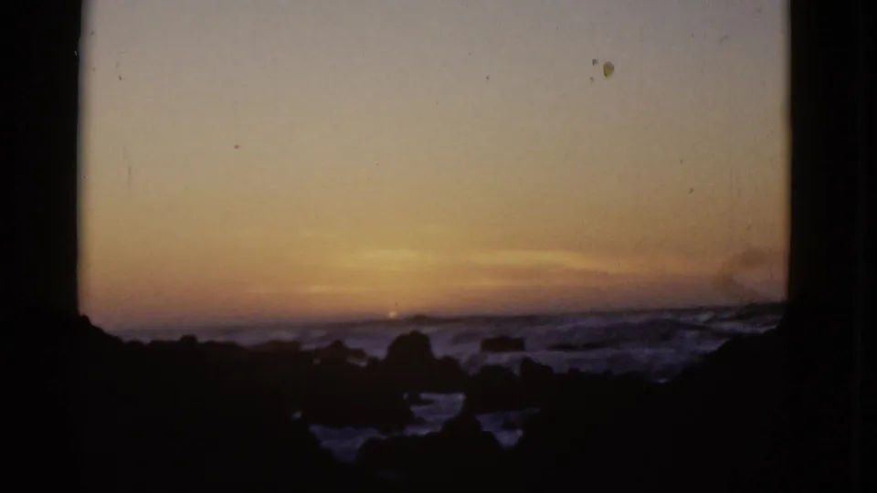 Soft 8mm frame from the 1952 San Francisco coast clip, with the sun nearly hidden behind haze and surf.