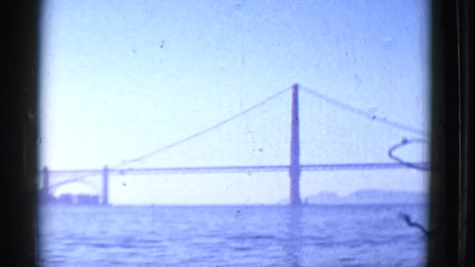 1952 San Francisco Bay view with the Golden Gate Bridge seen in soft focus across blue water under a pale sky.