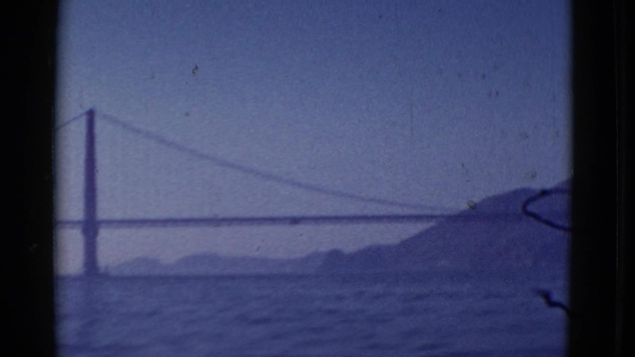 1952 San Francisco home-movie frame with a likely Golden Gate Bridge span, bay water, and a dark hillside at right.