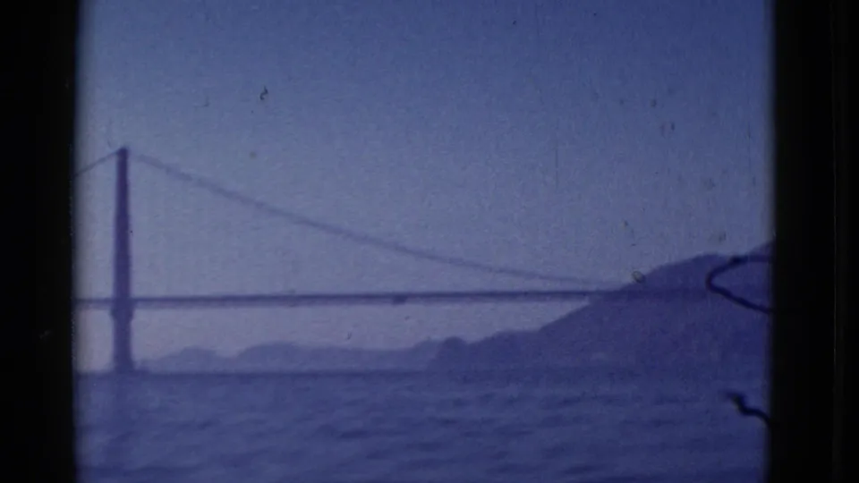 1952 San Francisco home-movie frame with a likely Golden Gate Bridge span, bay water, and a dark hillside at right.