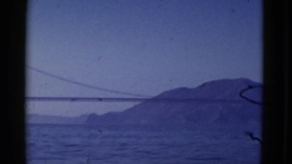 1952 San Francisco 8mm frame showing part of a suspension bridge and bay, with a large hill beyond the water.