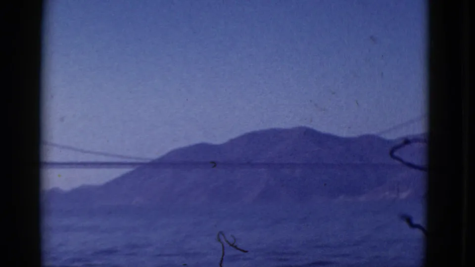 1952 San Francisco home-movie frame looking across bay water toward hills, with a bridge edge at the far side.