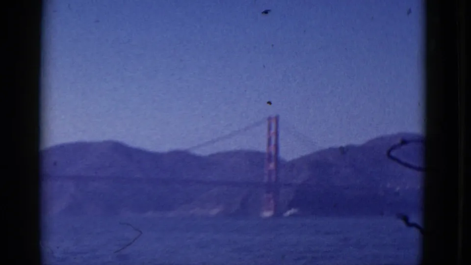 Distant 1952 home-movie view of the Golden Gate Bridge across the bay, softened by haze, grain and blue color shift.