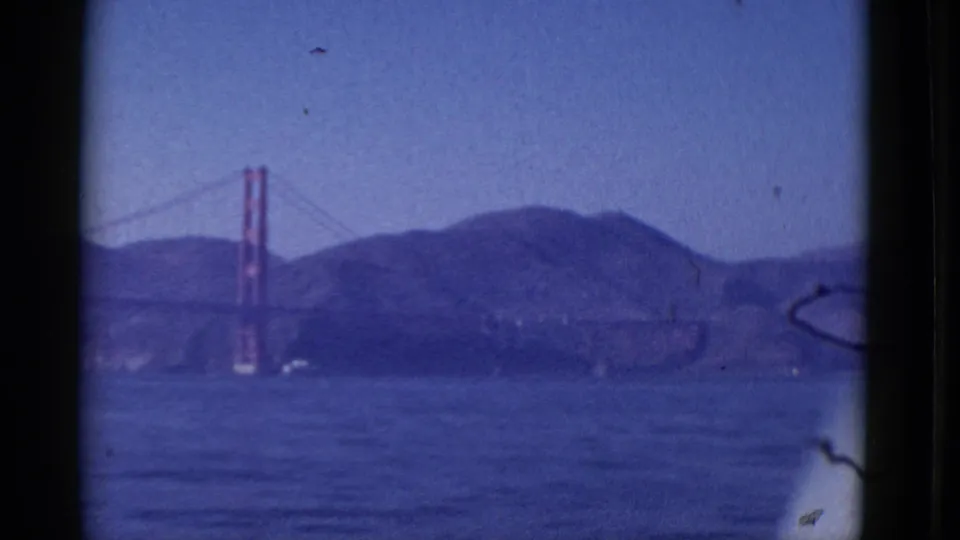 Final 1952 8mm frame of the Golden Gate Bridge across San Francisco Bay, with blue haze, hills and dark viewfinder-like edges.