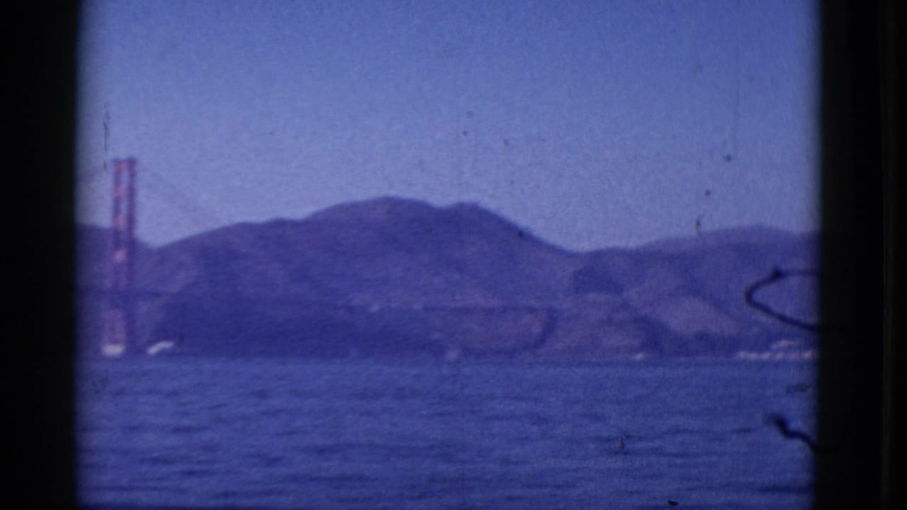 1952 8mm view across San Francisco Bay toward the Golden Gate Bridge and low hills, framed by dark film edges.