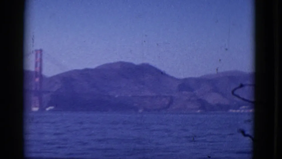 1952 8mm view across San Francisco Bay toward the Golden Gate Bridge and low hills, framed by dark film edges.