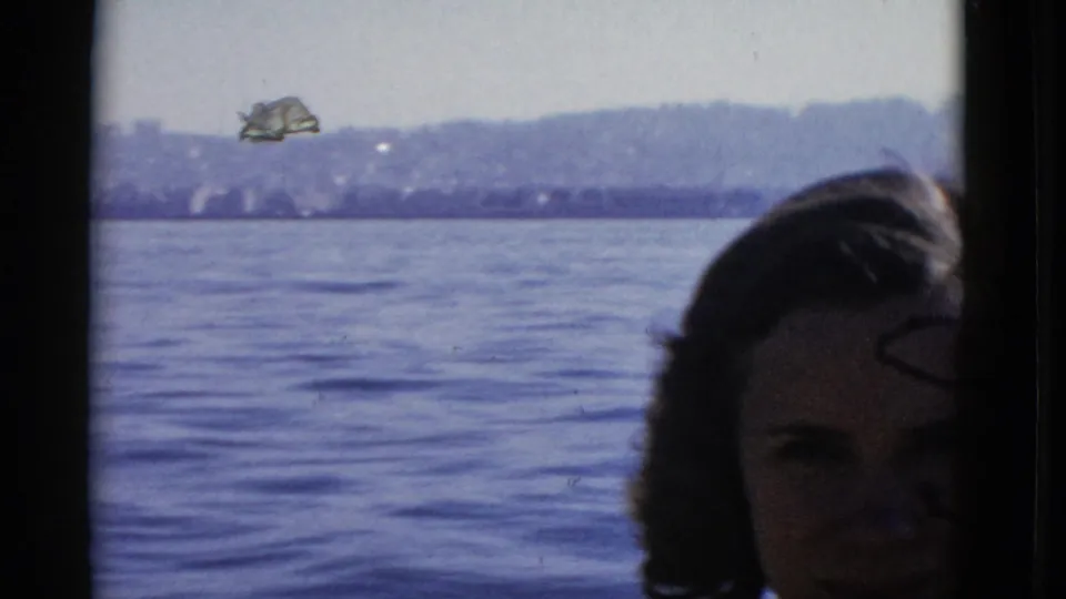 The woman is partly low in frame as the handheld 8mm camera looks across San Francisco Bay toward the shoreline.