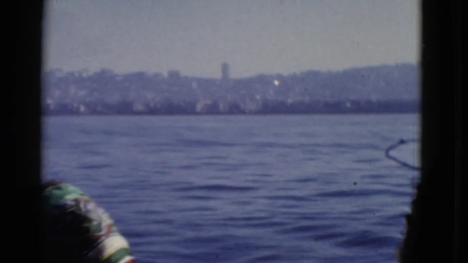 1952 8mm boat view across San Francisco Bay toward a distant shoreline, with a partial figure at the lower edge.