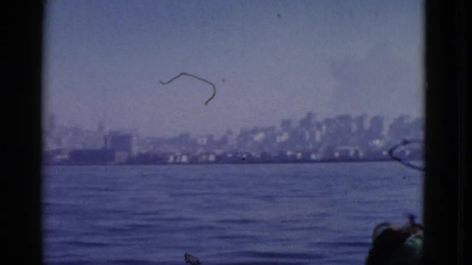 1952 bay view toward San Francisco, showing a soft waterfront skyline, pale sky, film dust, and a partial passenger at the lower edge.