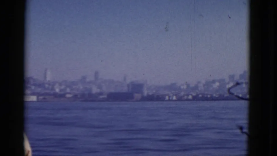 Distant San Francisco skyline across the bay, softly rendered on 8mm film with dark borders and a partial passenger head below.