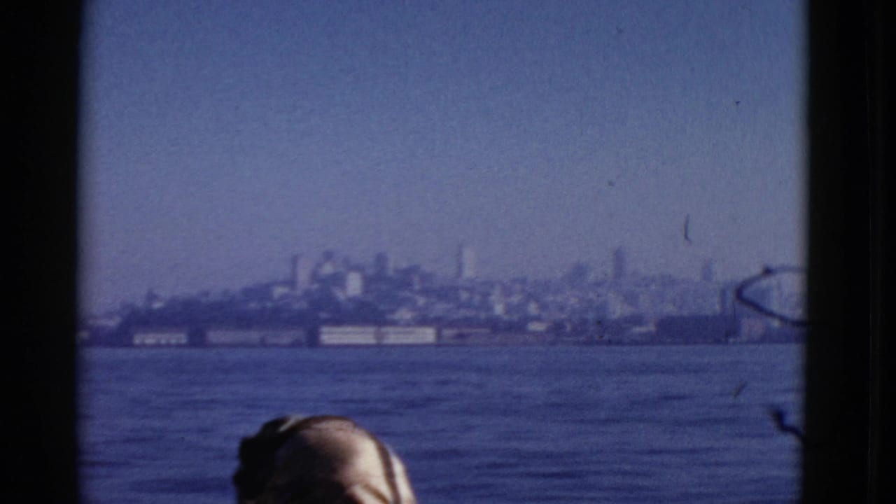 Distant shoreline across blue water with the top of a passenger's head at the bottom edge.