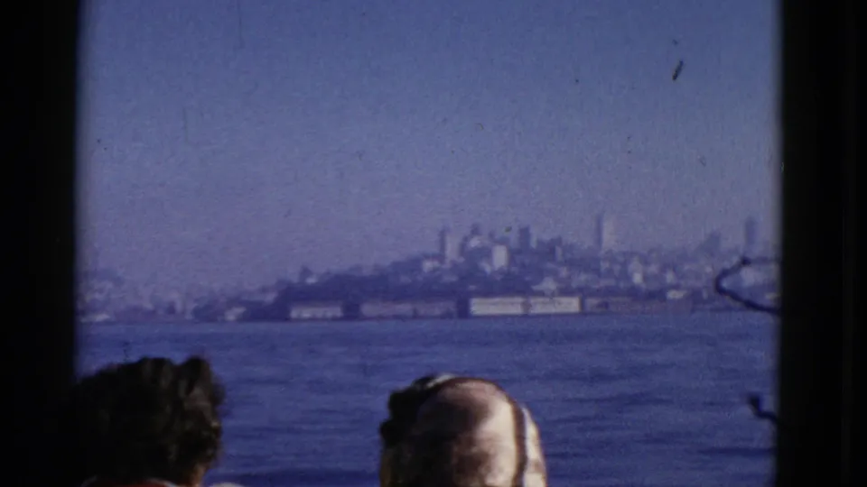 Two passengers on a boat look toward the San Francisco shoreline across the water in 1952 home-movie footage.