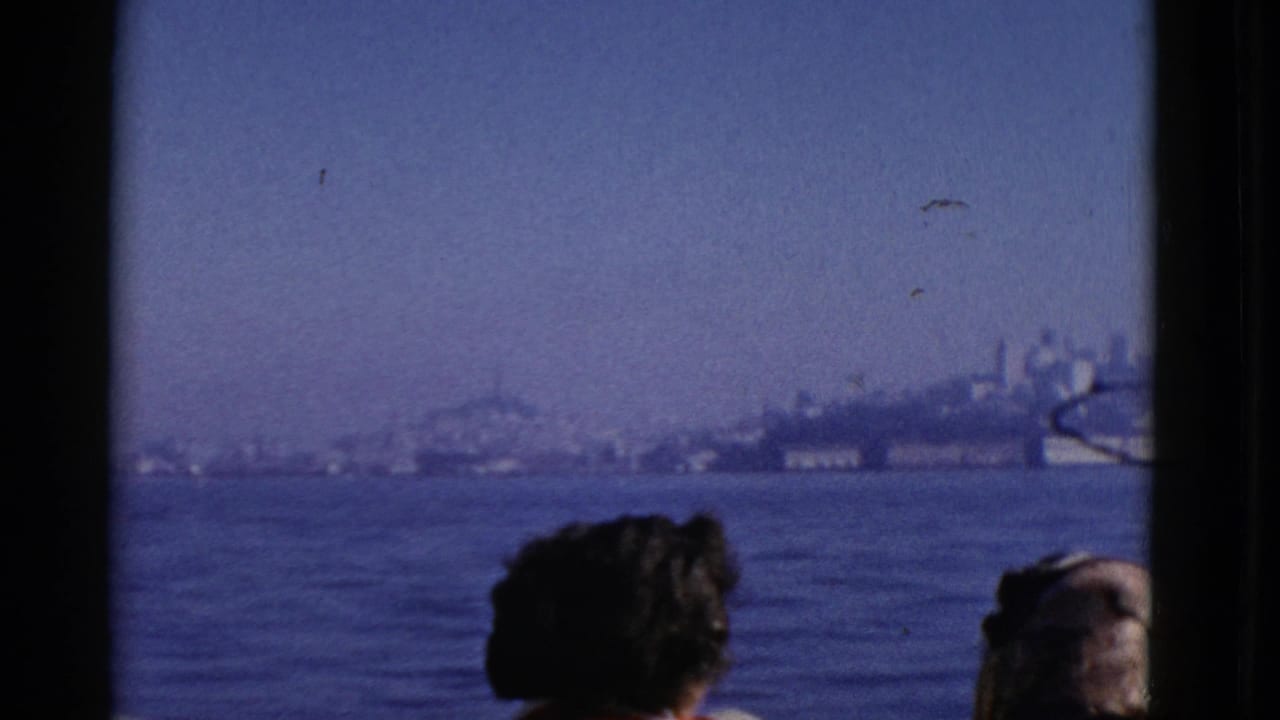 1952 8mm home-movie frame of passengers viewed from behind as a boat window frames hazy San Francisco Bay and distant shoreline.