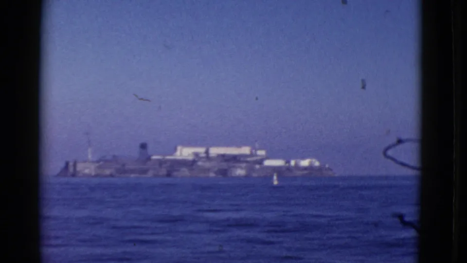 1952 San Francisco Bay frame showing Alcatraz Island across open water, bordered by the dark edge of a boat window and visible film wear.