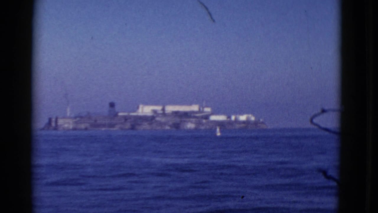 1952 8mm view of Alcatraz Island seen from across San Francisco Bay, with blue water and a small buoy in the foreground.
