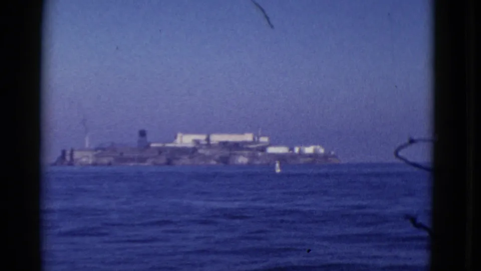 1952 8mm view of Alcatraz Island seen from across San Francisco Bay, with blue water and a small buoy in the foreground.