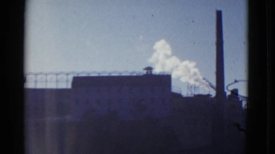 1952 San Francisco footage shifts to an industrial-looking structure with railings, barbed wire, a tall stack, and white smoke.