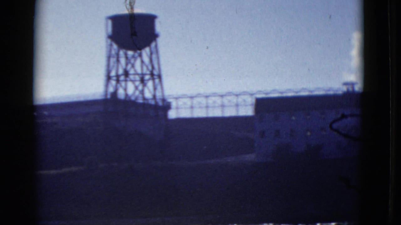 Water tower above shadowed industrial buildings and a fence-like roofline.