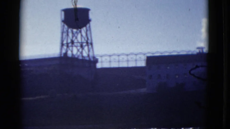 1952 San Francisco industrial site with a tall water tower silhouetted above low buildings and a roofline fence or railing.
