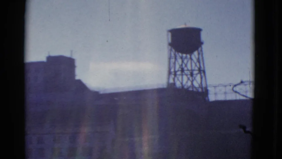 1952 San Francisco industrial complex with a silhouetted water tower, roofline railing, dark buildings, and visible color shift.