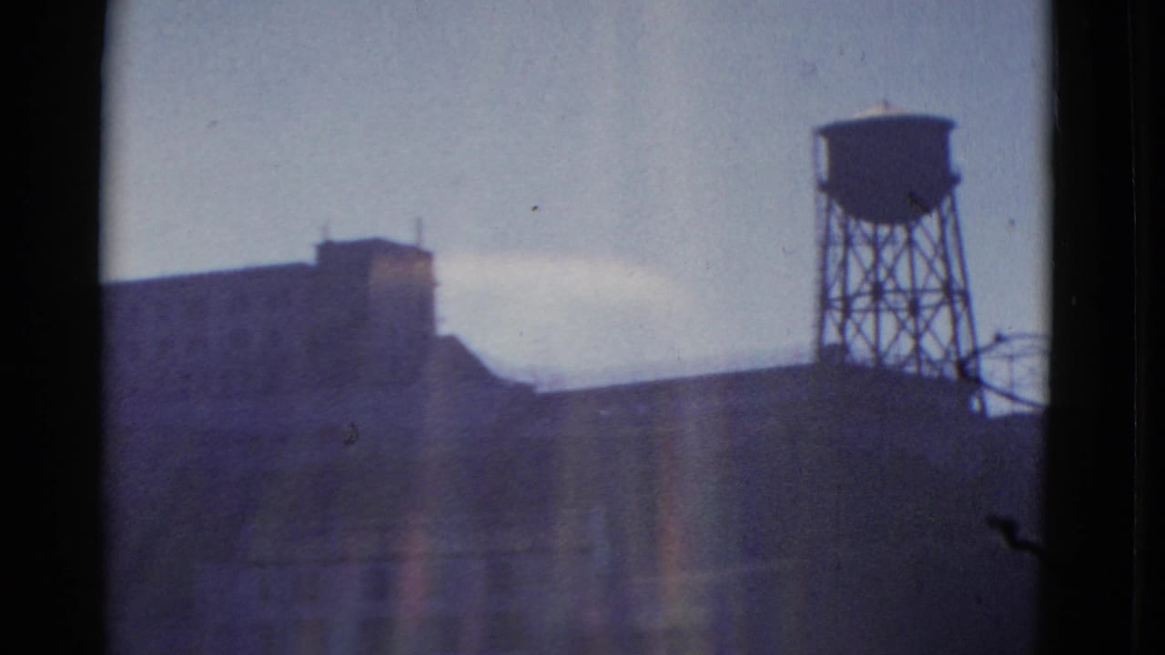 1952 San Francisco home-movie frame showing a distant masonry building and elevated water tower through a dark-edged window view.