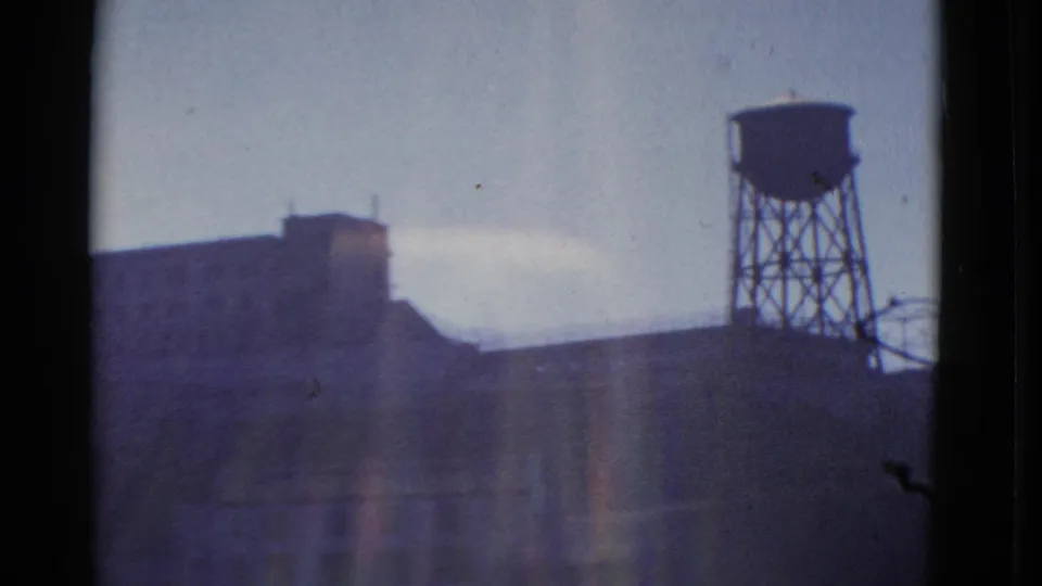 1952 San Francisco home-movie frame showing a distant masonry building and elevated water tower through a dark-edged window view.