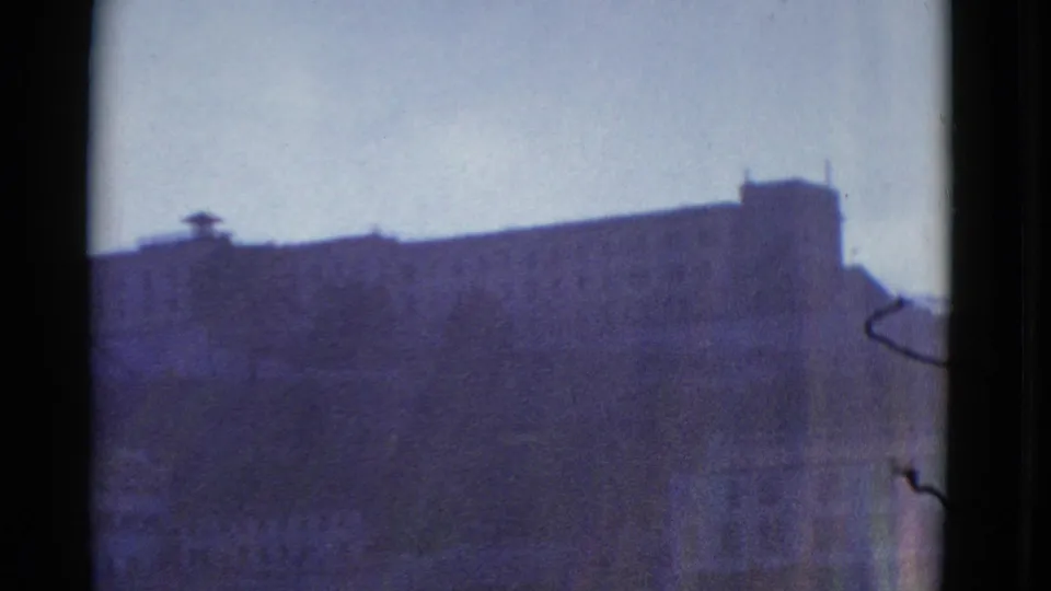 1952 San Francisco 8mm frame with a distant stone or masonry building roofline, pale sky, and blurred lower facade details.
