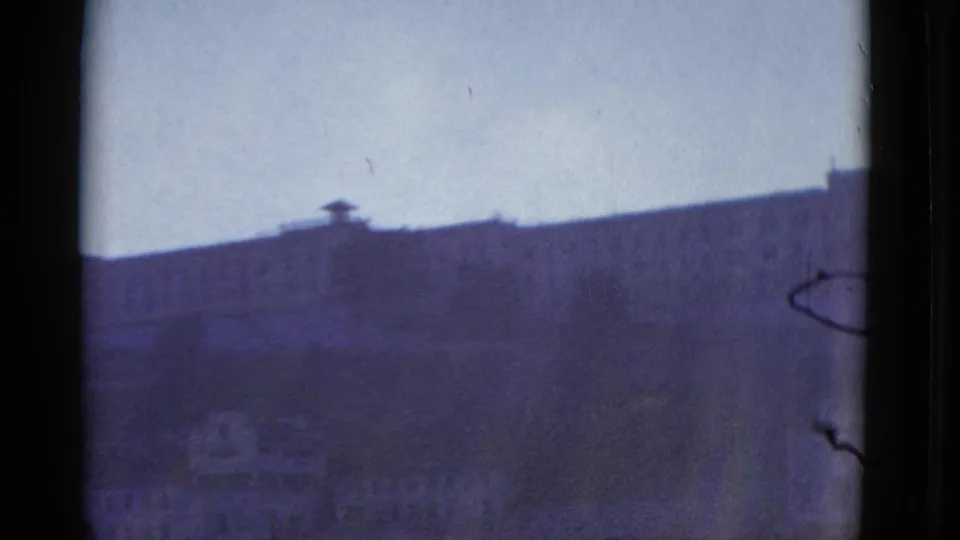 Final 1952 San Francisco home-movie frame showing a distant flat-roofed building under pale sky with soft 8mm color shift.