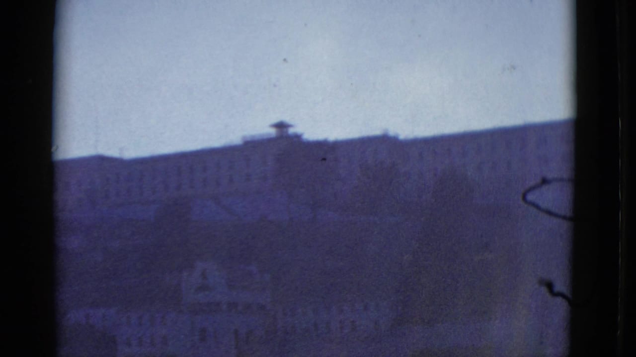 Distant hillside building seen through dark film borders under a pale sky.