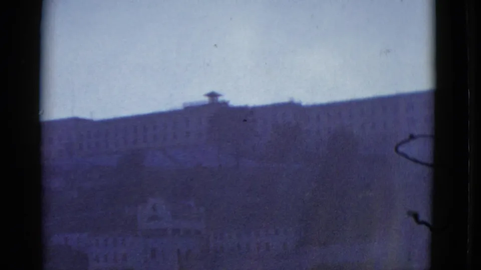 1952 San Francisco home-movie frame showing a distant hillside building and pale sky through dark gate or window-like borders.