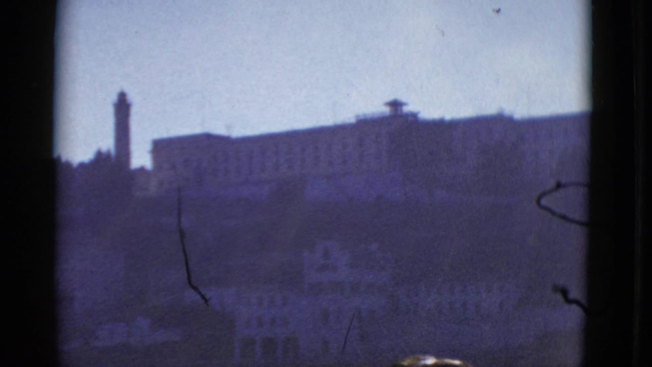 Tall tower and large hillside building silhouetted in a soft blue-purple frame.