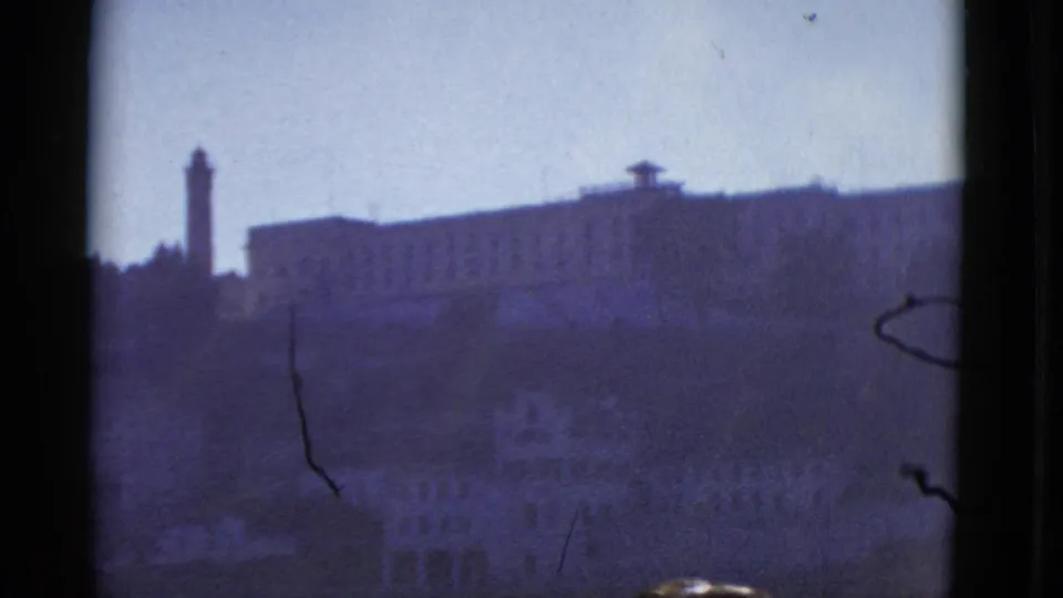1952 San Francisco frame with a tall tower beside a large hillside building, seen in soft focus through aged 8mm film.