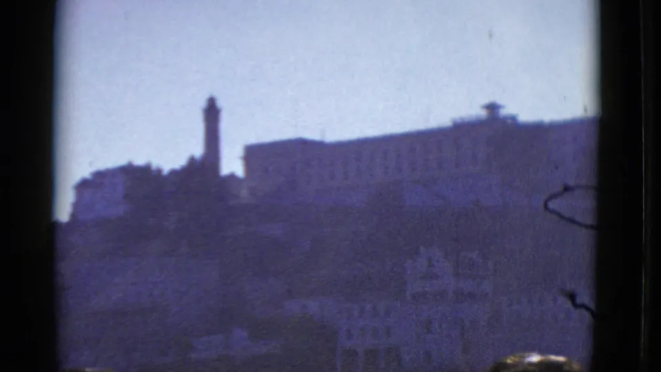 1952 San Francisco hilltop view with a tower, large building, and faint lower city structures in purple-shifted 8mm footage.