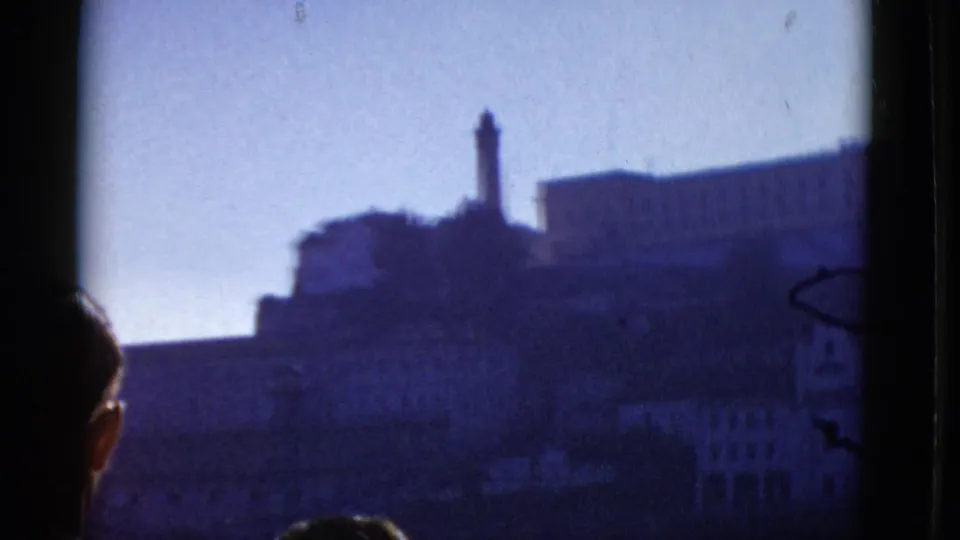 1952 San Francisco home-movie frame with a partial foreground head below a distant tower and hillside building.