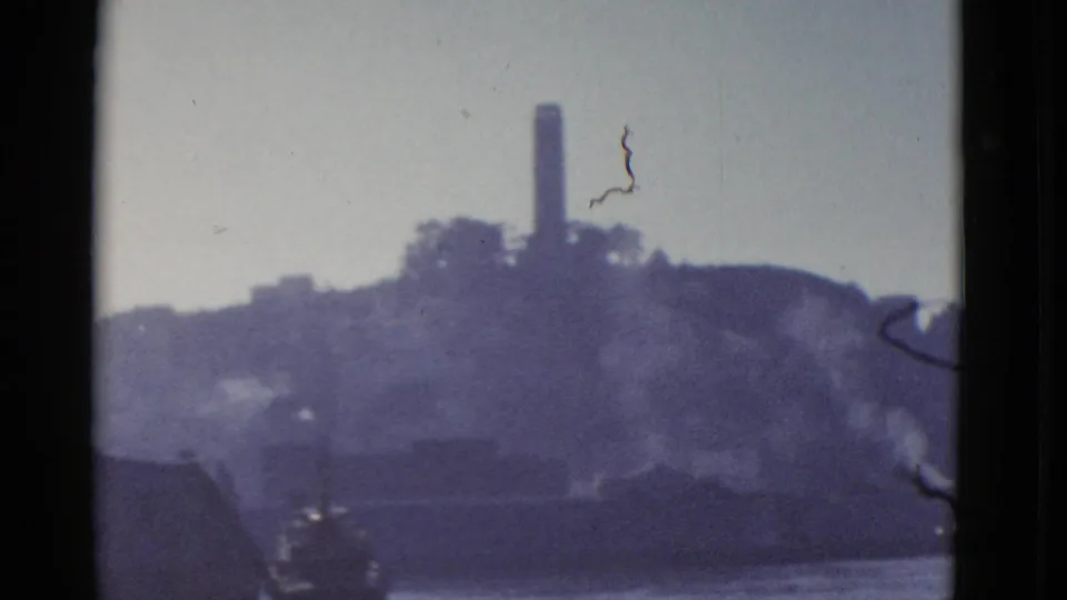 Soft 1952 8mm view of Alcatraz Island from the water, with rock, buildings, and tower visible.