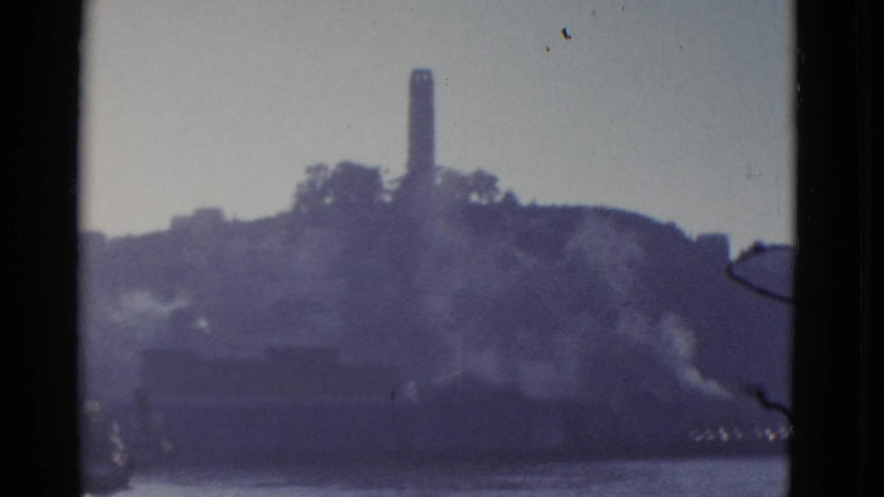 1952 San Francisco home-movie frame showing a distant hilltop tower above the bay with soft haze and dark projector-edge borders.