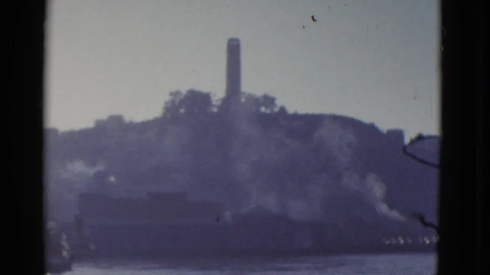 1952 San Francisco home-movie frame showing a distant hilltop tower above the bay with soft haze and dark projector-edge borders.