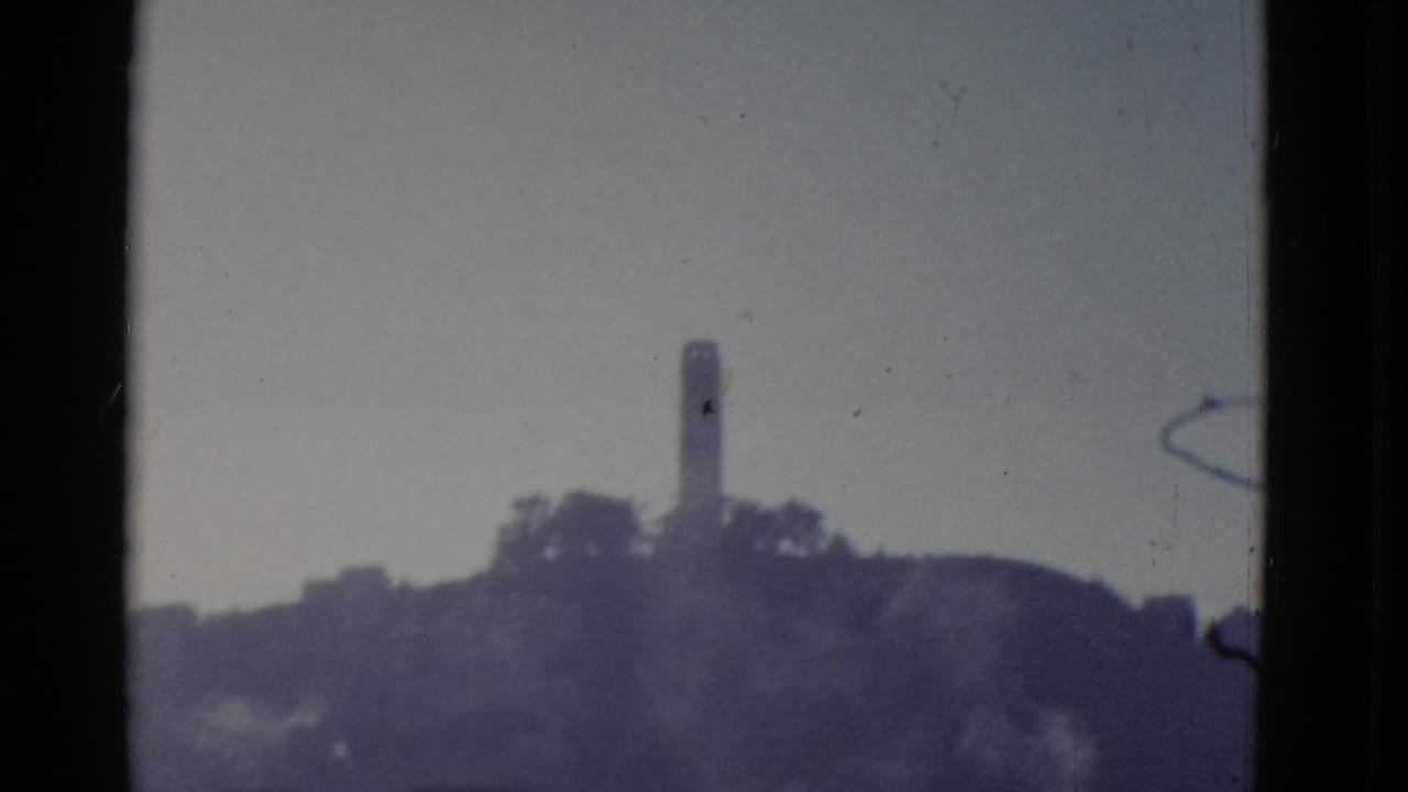 Hilltop tower seen across haze with dark vertical film borders.